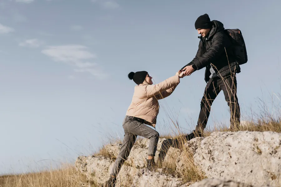 Two people climbing a hill, one helping the other up